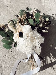 a bouquet of white flowers and greenery is tied up on the ground with a ribbon