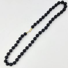 This onyx bead necklace features 8mm black onyx beads measuring 16 inches in length and with a 14 Karat yellow gold clasp. Black Onyx Necklace With Gemstone Beads, Black Single Strand Necklace, Formal Black Necklace With Gemstone Beads, Black Onyx Round Bead Necklace, Black Onyx Single Strand Jewelry, Formal Onyx Beaded Necklaces With Polished Beads, Formal Onyx Beaded Necklace With Polished Beads, Black Single Strand Pearl Necklace, Onyx Bead Necklaces With 8mm Round Beads