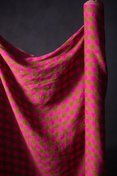 a pink and yellow checkered fabric is draped in front of a black background,