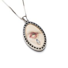 Designed and produced by WM Design. The Tearful Whisper Hand-Painted Sterling Silver Eye Pendant Necklace is an evocative piece that captures emotion through intricate artistry. Featuring a meticulously hand-painted eye with a single teardrop, this pendant speaks to vulnerability, resilience, and quiet strength. Encased in a sterling silver oval frame adorned with delicate dotted accents, the design has an antique-inspired elegance that enhances its timeless appeal. Weighing approximately 15-17 Teardrop Pendant Necklace, Eye Pendant Necklace, Silver Eye, Mens Jewelry Necklace, Forever Jewelry, Antique Inspiration, Eye Pendant, Jewelry Ring Box, Oval Frame