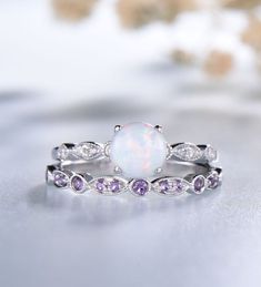 a white opal ring with purple and white stones on it's sides, sitting on top of a table