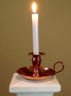 a lit candle sitting on top of a white table next to a metal bowl with a handle