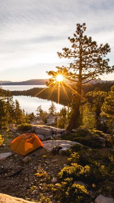 a tent pitched up on the side of a mountain overlooking a lake and forest at sunset