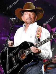 a man with a cowboy hat holding a guitar and singing into a microphone at a concert