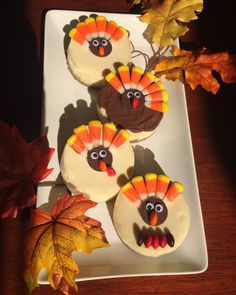 three cupcakes decorated like turkeys on a white plate with autumn leaves in the background