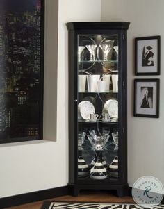 a glass cabinet with wine glasses and plates in front of pictures on the wall behind it