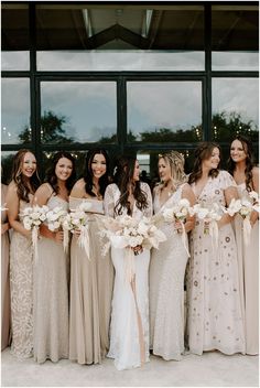 a group of women standing next to each other in front of a window holding bouquets