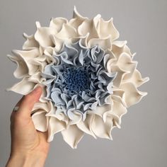 a person holding a paper flower in their left hand, on a gray background with white and blue petals