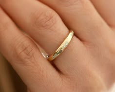 a woman's hand with a gold wedding band and diamond ring on her finger