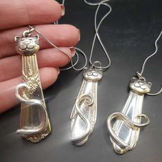 three silver pendants with cats on them are being held by someone's hand