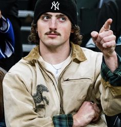 a man wearing a new york yankees hat pointing to the side while sitting in a crowd