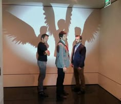 three people standing in front of a large screen with the shadow of two birds on it