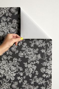 a person's hand on top of a black and white wallpaper with flowers