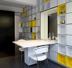 a kitchen with yellow and white shelving next to a dining room table in the center