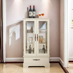 a white cabinet with wine bottles and glasses on it in a room that has beige walls