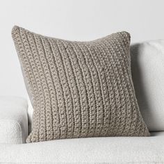 a white couch with a knitted pillow on it's back and the cushion is made out of fabric