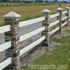 a white fence with stone pillars and posts in front of an open field on a sunny day