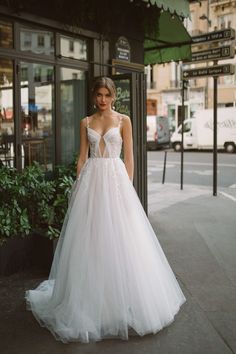 a woman in a wedding dress is standing on the sidewalk near a building and looking off into the distance