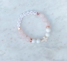 This beautiful personalized beaded bracelet is made with Rose Quartz ( Pink), Aquamarine (Blue) or Alabaster (White),  Howlite Cross and copper beads.   These bracelets are the perfect addition for your special occasion as a favour for a baptism, christening, communion, wedding shower, confirmation or any special or religious occasion.   DETAILS: ♡ Each bracelet comes with letter beads, 10 to 12 - 10MM beads and a Howlite Cross.  ♡ Select bracelet size in drop down.  Custom sizes available, specify in personalization section.  Select size or measure your wrist and add between 1/4 to 1/2 inch depending on your preference. ♡ Made with White Alabaster and Aquamarine or Rose Quartz beads and copper details. ♡ Each bracelet comes packaged beautifully with a jewellery bag. Great as a favour or a Birthday Bracelets With Name On Round Beads, Personalized White Beaded Bracelets For Mother's Day, Custom Name Pink Charm Bracelet For Mother's Day, Personalized White Beaded Bracelets As Gift, Personalized White Beaded Bracelets Gift, Personalized Beaded Bracelets As Gifts, Customizable Pink Charm Bracelet As Gift, Customized White Round Bracelets, Customizable Charm Bracelet For Birthday