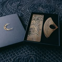 an open box with a card and a crescent brooch in it on a bed