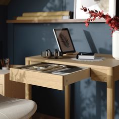 a wooden desk with a laptop on it and a flower in a vase next to it