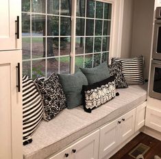 a window seat with several pillows on it in front of a stove and microwave oven