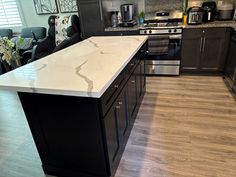 a kitchen with black cabinets and white marble counter tops, stainless steel appliances and wood flooring