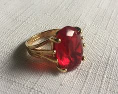 Elegant solitaire red ring set in a gold setting. The gemstone measures .75" by .5"  and it's set in a 18 Kt Electroplated Gold setting. (It says 18 Kt GE inside.) Size 5.75 or maybe 6. Please know that if you don't like the way the ring fits, you can return it; you pay for the shipping, but there's no restocking fee or questions asked, I just refund the ring's cost to you. Please take a look at my storefront at: https://www.etsy.com/shop/FabFinds42?ref=seller-platform-mcnav I have a wide select Red Crystal Party Ring, Red Open Ring Crystal Ring As Gift, Red Crystal Open Ring For Gift, Red Crystal Ring For Valentine's Day, Gift Red Crystal Open Ring, Red Open Ring Jewelry Gift, Red Open Ring Jewelry For Gifts, Red Rings For Valentine's Day Formal Occasion, Formal Red Rings For Valentine's Day