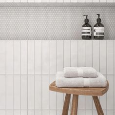 two white towels are sitting on a stool in front of a tiled wall with soap dispensers