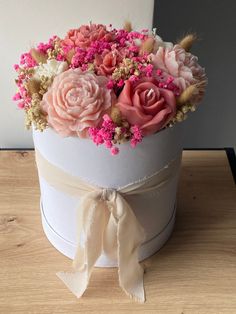 a white hat with pink flowers in it sitting on a wooden table next to a wall