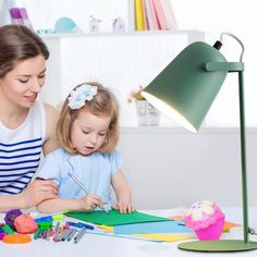 a woman and child are sitting at a table in front of a lamp with cupcakes on it