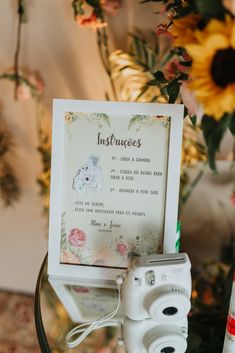 a white camera sitting on top of a table next to a vase with sunflowers