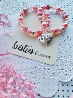 two bracelets with pink beads and silver heart charms on top of a doily