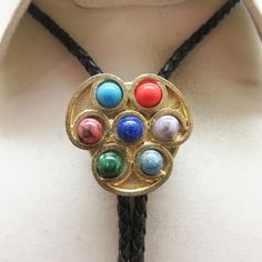 This cool Faux Gemstone bolo tie works for a woman with a sense of style. It is goldtone metal with small semiprecious cabochons in excellent condition. It measures 1 3/8ths inches tall by 1 3/8ths inches wide. It is placed on a brand new 36 inch long braided black leather string tie with  goldtone metal end caps. All pieces are in great condition.  This was handmade in our very own Montana rock shop, Rockin' JK Designs.  We will mail this to you in a lovely gift box for easy gift giving or safe Adjustable Metal Lariat Necklace For Formal Occasions, Adjustable Southwestern Bolo Tie For Formal Occasions, Southwestern Style Adjustable Bolo Tie For Formal Occasions, Southwestern Style Formal Bolo Tie, Vintage Lariat Jewelry With Sliding Knot, Vintage Adjustable Bolo Tie For Formal Occasions, Southwestern Jewelry With Adjustable Chain, Southwestern Style Jewelry With Adjustable Chain, Adjustable Gold Cabochon Necklace