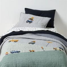 a bed with cars and trucks printed on the comforter, along with two pillows