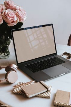 an open laptop computer sitting on top of a white table next to pink flowers and jewelry