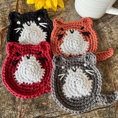 three crocheted cat coasters sitting on top of a table next to a yellow flower