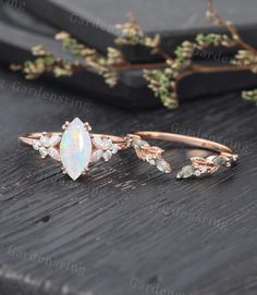 an opal and diamond ring sitting on top of a wooden table next to flowers