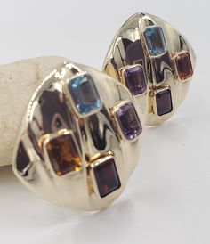 Title: Multicolor Gemstones Round Corner Square 14KT Yellow Gold Omega Clip Earrings Designer: Unbranded Material14KT Stamped Style: Vintage Gemstone Details All measurements are approximate and may vary slightly from the listed dimensions.1ar Approximately 5mm x 4mm each 1Amethyst Rectangular 1 Blue Topaz Rectangular 1 Orange Citrine Rectangular 1 Garnet Rectangular Estimated Measurements of the item30.23mm x 20.23mm x 5.83mm Estimated Total Weight of the Item DWT: 7.6 Grams: 11.7 Condition: Pr Luxury Multicolor Earrings With Gemstone Accents, Luxury Multicolor Earrings For Formal Occasion, Yellow Gold Earrings With Gemstone Accents For Party, Evening Multi-stone Round Earrings, Multicolor 17 Jewel Earrings For Party, Luxury Multicolor Earrings For Evening, Multicolor Gemstone Accented Fine Jewelry Earrings, Multicolor Gemstone-accented Fine Jewelry Earrings, Multicolor Gemstone Accented Earrings For Formal Occasions