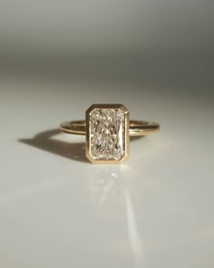 a yellow gold ring with a square cut diamond in the center on a white surface