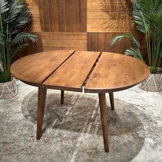 a round wooden table sitting in front of some potted plants