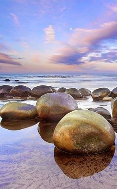 several large rocks sitting on top of a sandy beach next to the ocean at sunset