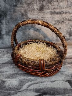 a wicker basket with hay in it sitting on a gray blanketed surface next to a wall