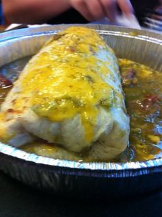 an enchilada in a foil pan on a table with a person sitting at a table