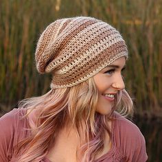 a woman with blonde hair wearing a knitted hat in front of some tall grass