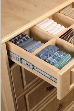 an open drawer in a kitchen with folded shirts and pants inside it on the bottom shelf