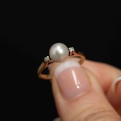 Elevate your style with this exquisite Vintage Cultured Pearl Ring adorned with two dazzling accent diamonds on either side. The centerpiece is a lustrous 7.20mm cultured pearl, exuding elegance and sophistication. Flanking the pearl are two, 2mm diamonds which add a touch of brilliance to this classic piece. Set in a beautifully scalloped base, the pearl is positioned prominently, creating a stunning focal point. The ring is marked with 14K and 18K stamps, along with a distinct maker's mark, si Wedding Pearl Ring With Single Diamond, Wedding Pearl Ring With Diamond, Classic Pearl Ring With Diamond, Classic Pearl Ring With Diamond Center Stone, Fine Jewelry Pearl Ring With Single Diamond For Anniversary, Classic Brilliant Cut Pearl Promise Ring, Classic Pearl Ring With Prong Setting, Classic Pearl Ring With Prong Setting In Diamond White, Timeless Pearl Ring With Prong Setting For Anniversary