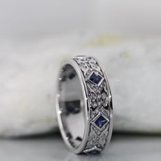 a white gold ring with blue sapphires and diamonds on the side, sitting on a rock