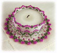 a white candle with pink and green beads around it on a white cloth covered table