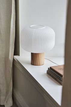 a white lamp sitting on top of a window sill next to a bookshelf